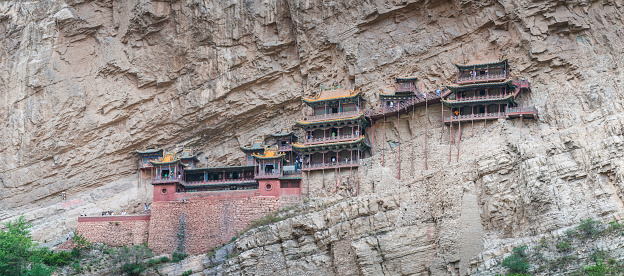 Datong, China - 23rd June 2009: Tourists exploring the vertiginous wooden pagodas of the Hanging Monastery Xuankong Temple built over a thousand years ago high on a mountain cliff in the Shanxi province of China. Composite panoramic image created from five contemporaneous sequential photographs.