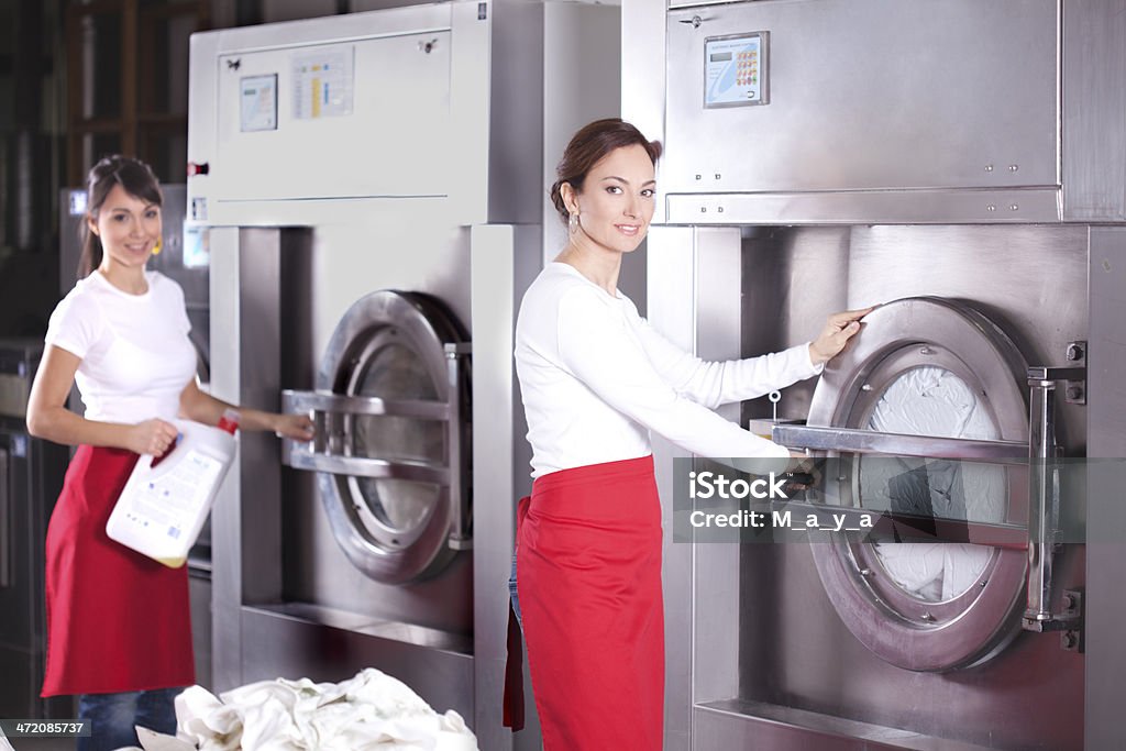 Laundry service. Workers in laundry service,preparing to pour detergent and washing machine to turn on. Adult Stock Photo