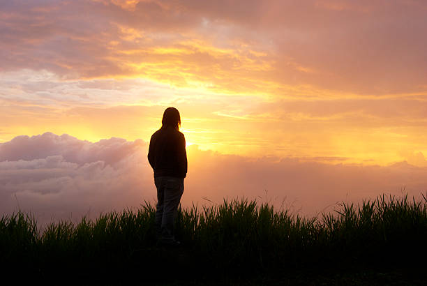 Man in silhouette standing on rock with sunset sky background. stock photo