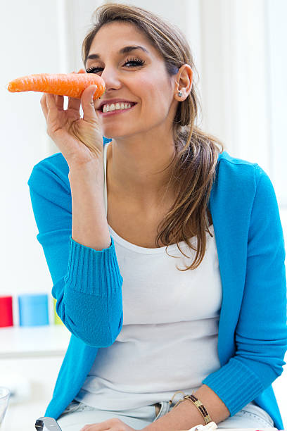 istock Young woman having fun with a carrot in the kitchen 472089205