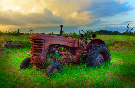 Old abandoned tractor on a farm with storm clouds in the background.