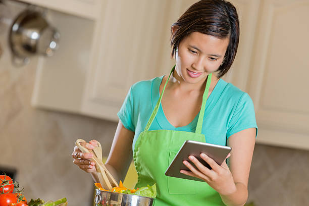 istock Young Asian woman cooking while reading recipe on digital tablet 472093337