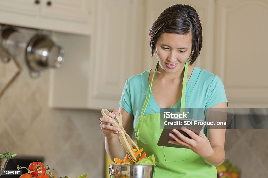 Asiatique femme lisant une recette sur tablette numérique et cuisine - Photo de Cuisiner libre de droits