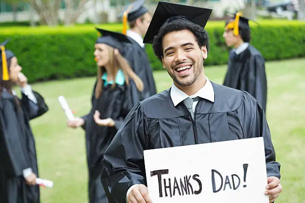 Photo of Excited high school or college graduate holding 'thanks dad
