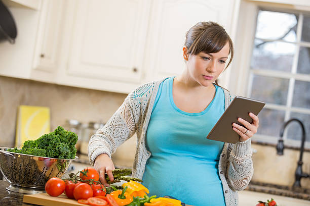 istock Pregnant mother reading recipe on digital tablet while cooking 472095089