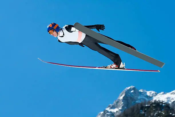 Side view of young male ski jumper during the long ski jump against the blue sky