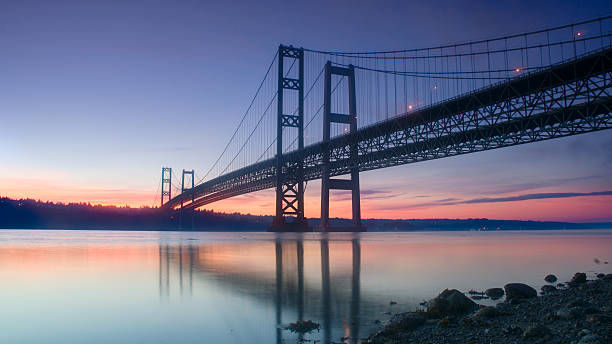 Sunset behind a dark bridge with still waters The Narrows Bridges taken at sunrise in Tacoma, WA, USA. tacoma photos stock pictures, royalty-free photos & images