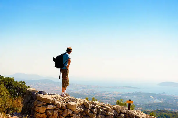 Backpacker standing on a wall high up over the mediterranean sea. Location: Mountains close to Toulon, France