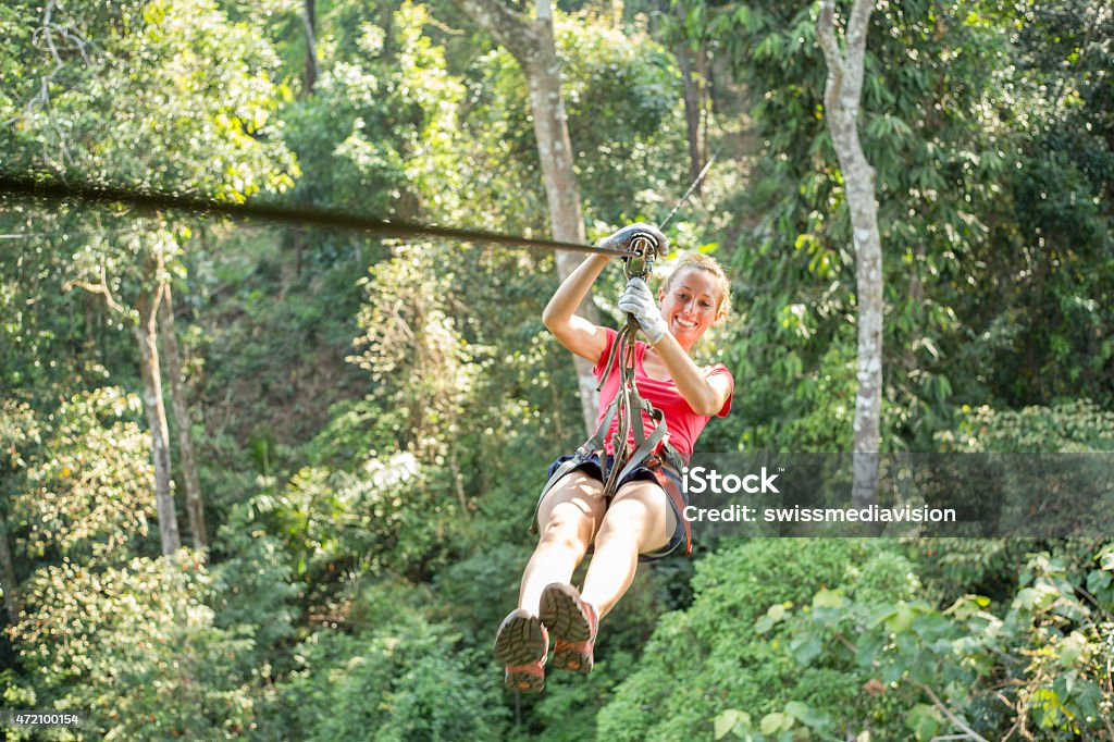 Happy adventurous woman on a zip-line crossing the jungle Young healthy woman enjoying zip-lining  on a canopy tour adventure in the rain forest in northern Laos, sunny summer day. Zip Line Stock Photo