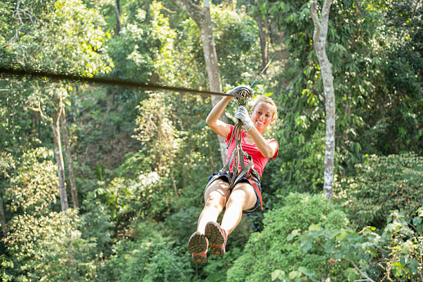 Happy adventurous woman on a zip-line crossing the jungle Young healthy woman enjoying zip-lining  on a canopy tour adventure in the rain forest in northern Laos, sunny summer day. canopy tour photos stock pictures, royalty-free photos & images