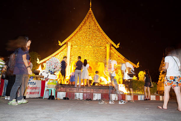 Chiang Mai, Thailand - February, 25th 2013: Buddhist night ceremony at temple Wat Phan Tao. People in foreground arewalking around shrine in center. People in center are praying to buddha. Around is fire and candle light.