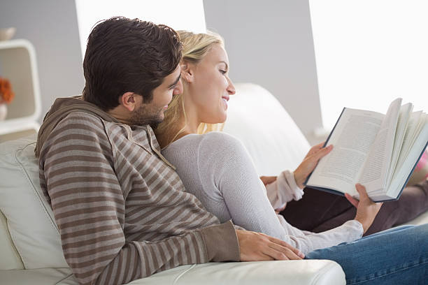 istock Happy couple sitting on couch reading a book 472100945