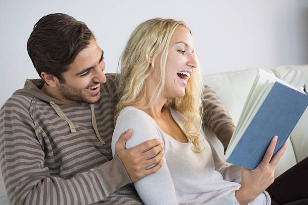 istock Laughing couple sitting on couch reading a book 472100953