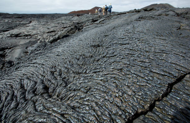 Tourist walking on black lava field Galapagos, Eguador - October 10, 2012: Tourist walking on black lava field at Sullivan Bay, Santiago Island in the wondrous Galapagos. isla san salvador stock pictures, royalty-free photos & images