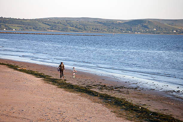 femme et enfant marchant sur la plage au bord de mer - wales beach editorial people photos et images de collection
