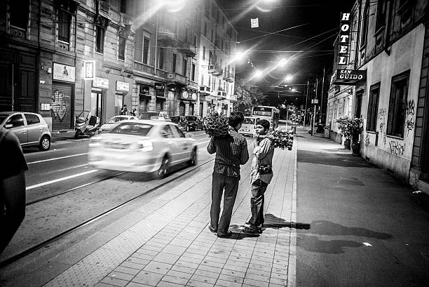 Milan, Italy - September 30, 2011: Flowers street vendors from Asia talking on the street during the night. They tend to approach couples and try to convice a boyfriend to buy a rose for his girlfriend.