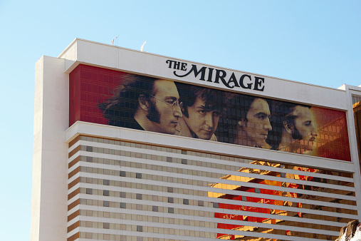 Las Vegas, Nevada, USA - December 1, 2013: View of top part of The Mirage which is a 3,044 room hotel and casino resort located on the Las Vegas Strip in Paradise, Nevada, United States. The hotel's distinctive gold windows get their color from actual gold dust used in the tinting process. The advertising of the Beatles  - John, Paul, George and Ringo show  -.LOVE, a Cirque du Soleil theatrical production involving remixes of The Beatles can be seen.  Also reflection ofb the other part of the hotel can be seen.