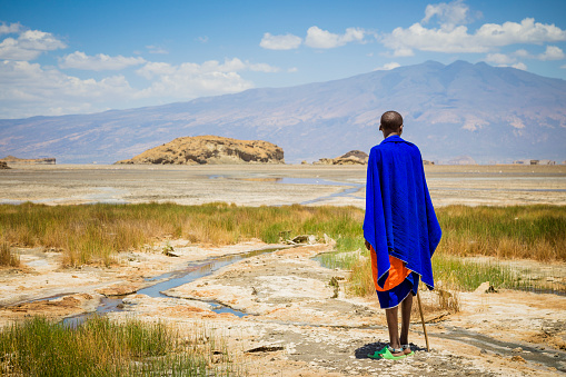 Lake Natron, Tanzania - October 04, 2013: Maasai man is standing at Lake Natron in Tanzania. He looks at the salt lake on the horizon where a herd of giraffes running across the lake.