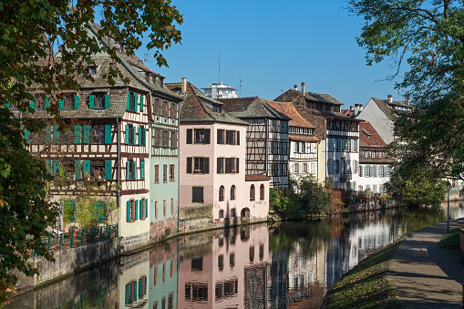 The Old Town of the french city Strasbourg, ( Bas-Rhin, Alsace, France ). Quarter La Petite France - a local landmark and UNESCO World Heritage. View onto ancient half-timbered houses at the waterfront. Reflections of the facades in the river Ill. Warm light of a sunny autumn day.