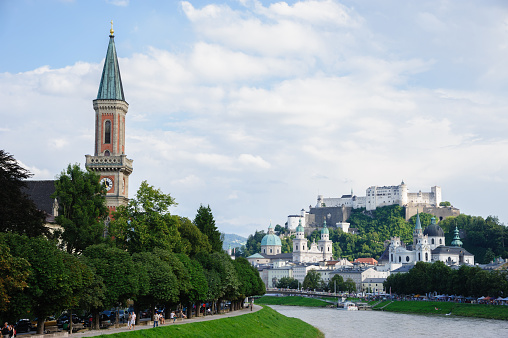 Salzburg, Austria - August 5, 2012: City of salzburg, in front there is the river Salzach, in the background the Salzburger Dom and the Festung Hohen Salzburg. Tourists walking on the bridge and riverside.