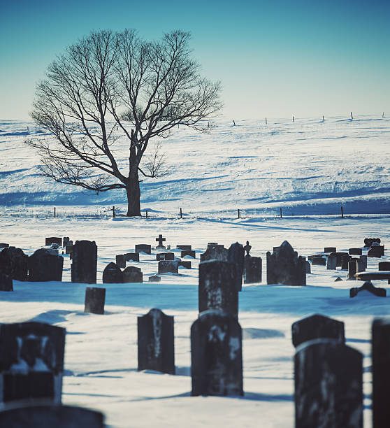 Cross shaped memorial gravestone at an angle covered in snow in cold winter