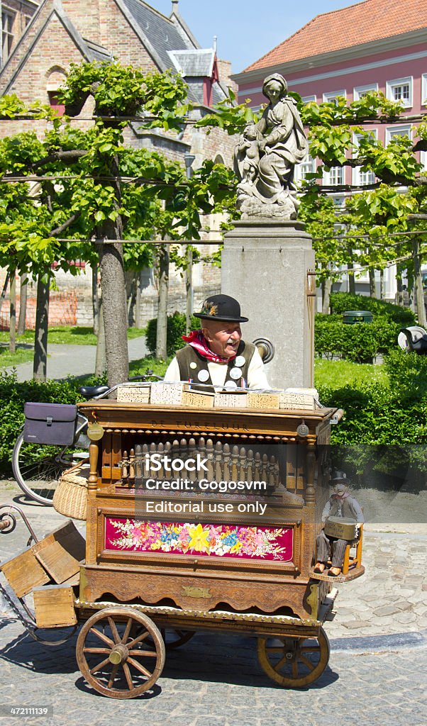 Street Musician Bruges, Belgium - June 4, 2013: Street musician playing an instrument in Bruges - top tourist destination of Belgium. In the background one can see the old statue of Bruges. Accordion - Instrument Stock Photo