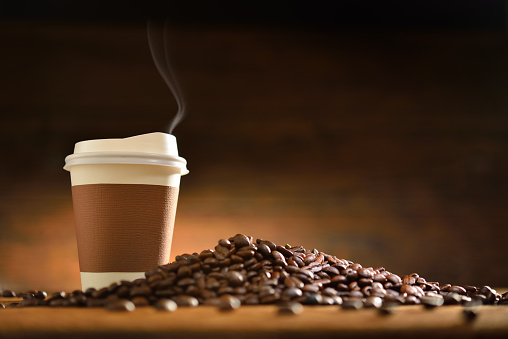 Paper cup of coffee with smoke and coffee beans on old wooden background