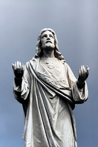 Old statue of Jesus Christ with his arms raised against grey background, from cemetery 1877, Sydney Australia, full frame vertical composition with copy space