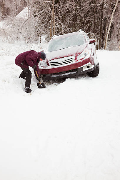 Man shoveling snow to rescue car from ditch Man trying to help his car out of the ditch by clearing a way out with his shovel. ditch stock pictures, royalty-free photos & images