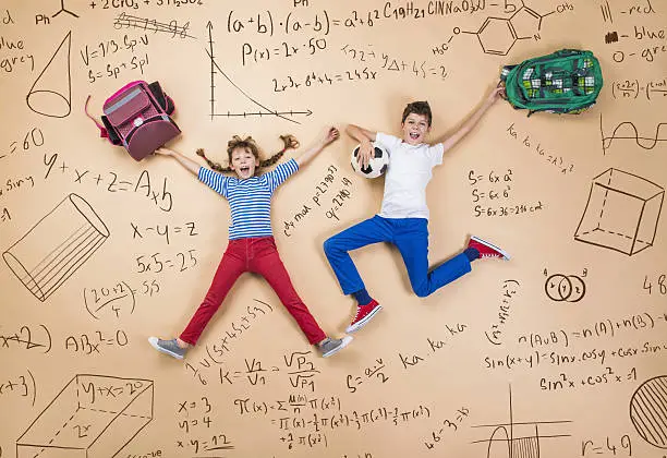 Cute boy and girl learning playfully in frot of a big blackboard. Studio shot on beige background.