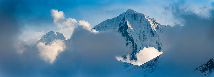 Clearing snow clouds swirling round the crisp white snow capped peaks and dramatic hanging glaciers of the unspoilt high altitude ridges of the Himalaya mountain wilderness, Nepal. ProPhoto RGB profile for maximum color fidelity and gamut.