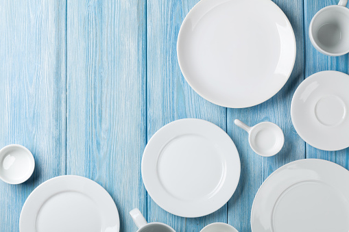 Empty plates and bowls on blue wooden background. Top view with copy space
