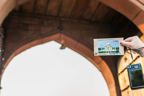 Agra, India - November 5, 2013:   A tourist holds up her admission ticket to the Taj Mahal, with the entrance archway in the background.