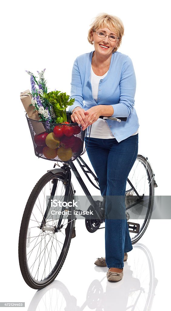 Active senior woman Portrait of smiling senior woman standing next to bicycle with grocery shopping in the basket. Studio shot, white background. Bicycle Stock Photo