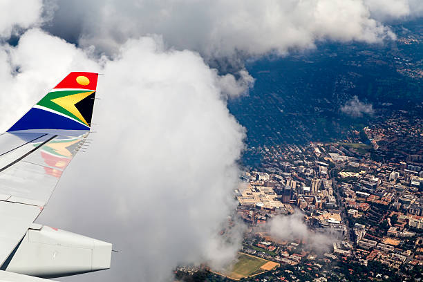 Johannesburg, South Africa - 10th January 2014: Airbus 330 wing from South African Airlines seen flying over Sandton City with clouds and the sun shinning on Sandton City below, in Johannesburg. Aeroplane close to landing at OR Tambo Airport.