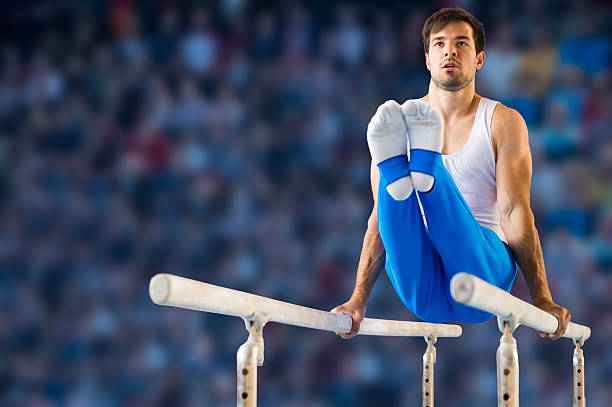 Male gymnast performing routine on parallel bars A young male gymnast performs a routine on the parallel bars.  He balances himself with only his straightened arms on the bars while his legs are held perpendicular to his body.  A crowd of spectators is blurred in the background. horizontal bar stock pictures, royalty-free photos & images