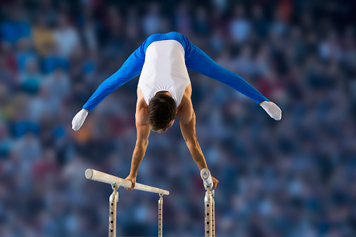 Rear view of young man performing short routine on parallel bars, artistic gymnastics