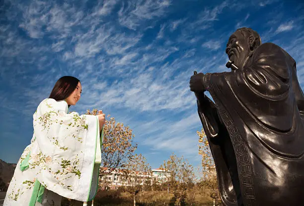 East asian teenage girl bowed to Confucius under blue sky wihte clouds