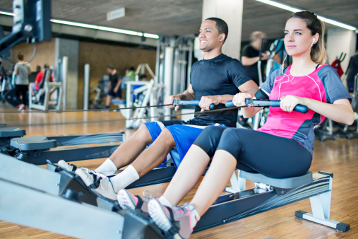 Two people at the gym doing exercises in the rowing machine.