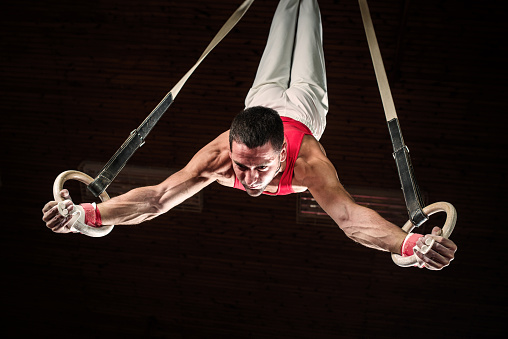 Low angle view of young man doing difficult exercises on gymnastics rings.   