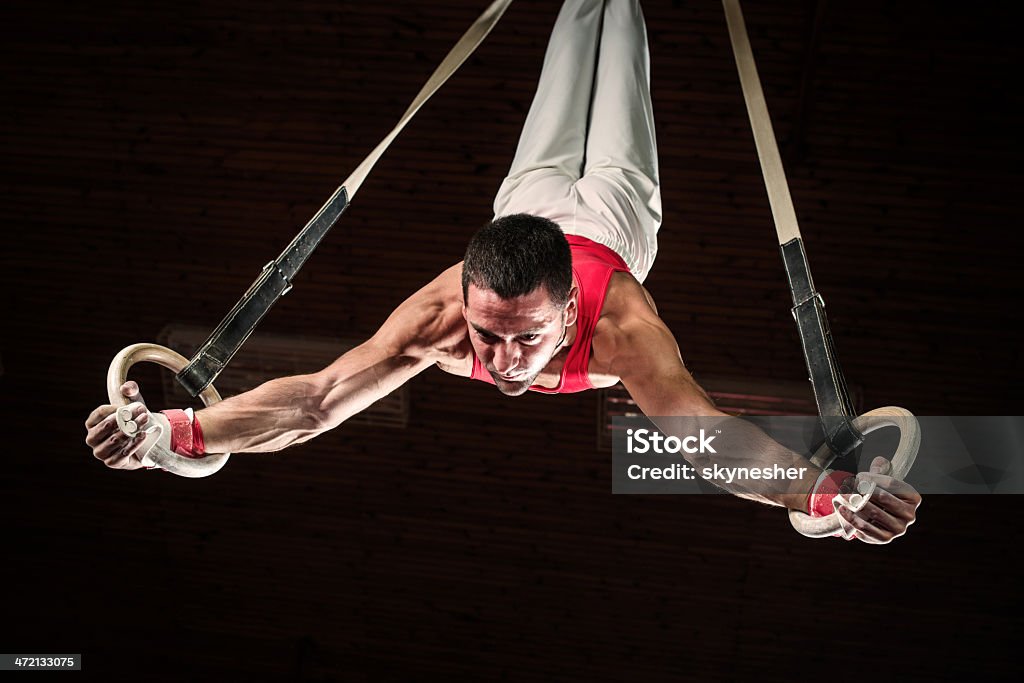 Male sportsman on gymnastics rings. Low angle view of young man doing difficult exercises on gymnastics rings.    Gymnastics Stock Photo