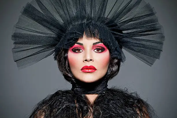 Fierce looking female model wearing a black tule headdress, extreme creative make-up. Black widow, black hair.