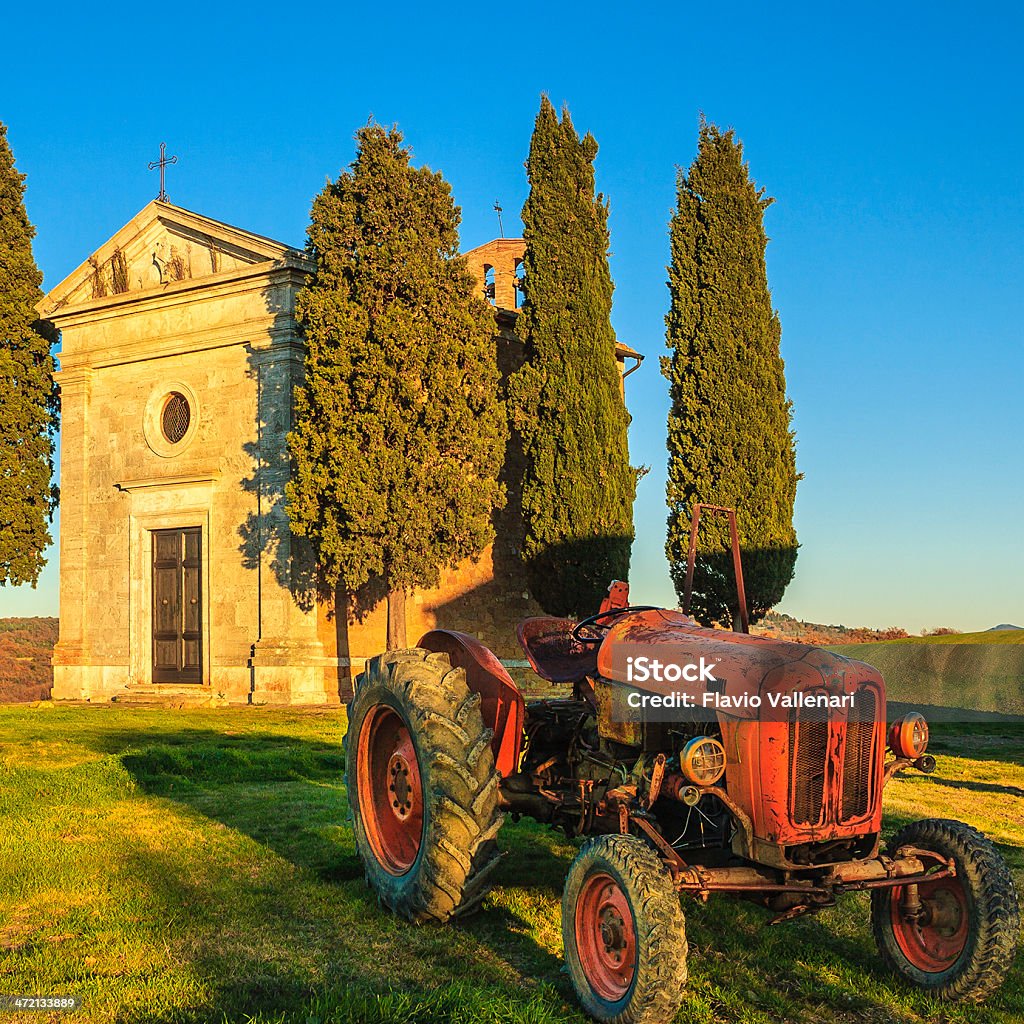 Red Old Tractor, Tuscany Red old tractor parked in front of the ancient church of Vitaleta, in the Tuscany countryside. Italy. Agricultural Field Stock Photo