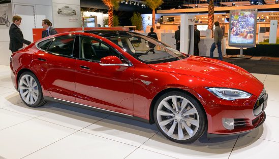 Brussels, Belgium - January 14, 2014: Red Tesla Model S full-sized electric five-door hatchback on display at the 2014 Brussels motor show. People in the background are looking at the cars.