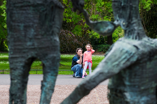 Dublin, Ireland - June 2, 2013: In Dublin's St. Stephen's Green, a father kneels beside his young daughter and points to a sculpture commemorating the Irish famine, explaining it to her. The sculpture is the work of Edward Delaney.