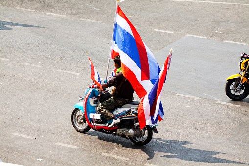 Bangkok, Thailand - January, 22nd 2014: A Thai man is driving ahead motorcycle convoi passing square Victory Monument and its roundabout. Man has many Thai flags around himself. Part of demonstrations in January 2014.