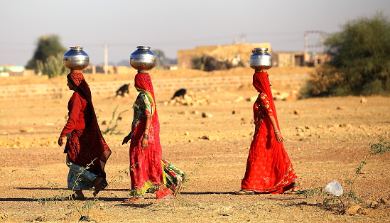 Rajasthan, India - February 27, 2013: women lugging a water pot on their head. Due to the lack of piped water, poor tribals have to fetch water from its natural sources.