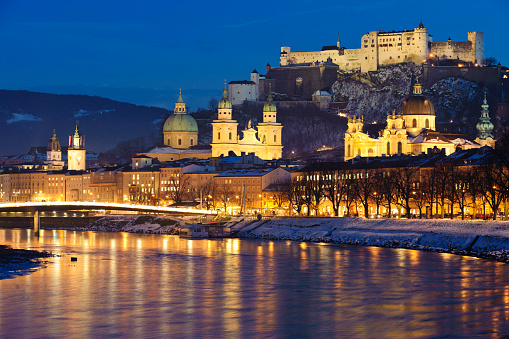 Salzburg, Austria - December 22, 2010: City Salzburg at christmas night in winter with river Salzach and the skyline of the medieval old town. The large building on the right side is a very famous church named Kollegienkirche. The double-towers in the middle belongs to the catholic cathedral and behind this dome you see the round cupola of a baroque church named Kajetanerkirche. The single tower with flags, at the left side, is part of the historical townhall. The huge ancient fortress named Hohensalzburg is located over the city and is its landmark.