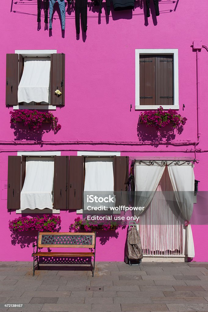 Pink Burano house with washing and bench, Venice, Italy Venice, Italy - June 5, 2012: Typically brightly coloured houses on Burano Island, Venice, Italy. Clothes hang from a washing line and flower boxes frame a bench outside Architecture Stock Photo