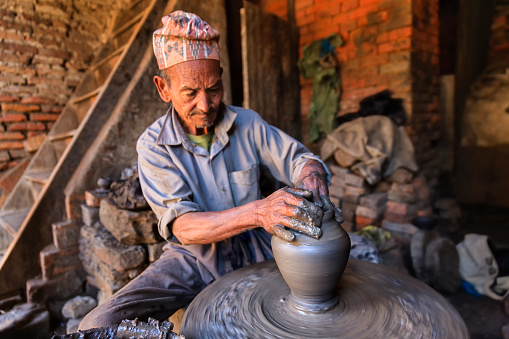 Nepalese potter working in his workshop on pottery square in Bhaktapur. Bhaktapur is an ancient town in the Kathmandu Valley and is listed as a World Heritage Site by UNESCO for its rich culture, temples, and wood, metal and stone artwork.